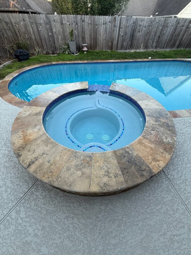 Round travertine spa with blue glass mosaic spilling into a pool