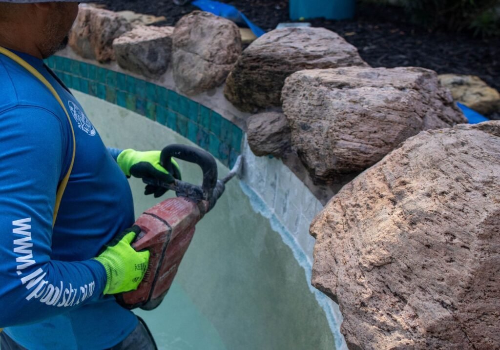 Living Water craftsman grinding the pool edge beside natural stone boulders